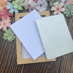 May include: Two metal stencils for crafting, one is silver and the other is white. Both stencils feature a repeating pattern of stitched lines forming geometric shapes.