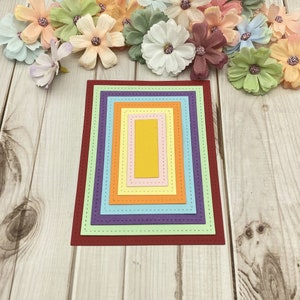 May include: A set of seven nested rectangular frames with stitched edges. The frames are in a rainbow of colors, starting with red and ending with yellow. The frames are on a light wood background.