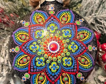 May include: A black Christmas ornament with a glittery finish, adorned with a vibrant, hand-painted mandala design. The mandala features a symmetrical pattern of colorful dots in red, orange, yellow, green, blue, and purple. A festive holiday decoration.