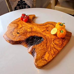 May include: A wooden chopping board with a distinctive shape and a warm brown hue. The board is decorated with red cherry tomatoes, a yellow bell pepper, an orange bell pepper, and a lemon slice. The natural wood grain is visible.