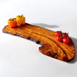 May include: A wooden serving board with a live edge, featuring a rich, warm wood grain. Two bell peppers, one orange and one yellow, sit on the left side. Four red tomatoes are on the right side. The board is on a white background.
