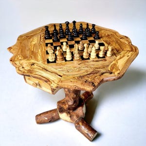 May include: A handcrafted wooden chess table with a unique, organic shape. The table features a built-in chessboard with black and white squares, and chess pieces are arranged for play. The table is supported by a natural wood base, showcasing the wood's grain and texture.