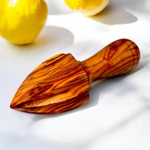 May include: A wooden citrus juicer with a pointed end and a rounded handle. The juicer has a reddish-brown grain pattern. Two yellow lemons are in the background.