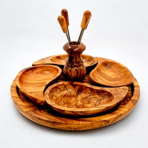 May include: A wooden serving tray with five compartments and a central holder for four small forks. The tray and holder are made of olive wood, showcasing a natural wood grain pattern. The forks have wooden handles.
