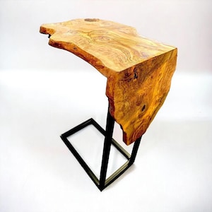 May include: A live edge side table with a natural wood top and a black metal base. The wood top is approximately 76 cm long and features a unique grain pattern with shades of brown and gold. The table is designed for indoor use.
