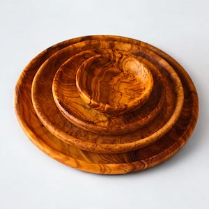 May include: Four wooden bowls of varying sizes nested together. The bowls are made of a light brown wood with a prominent grain pattern. The largest bowl is a shallow dish, while the smallest is a deep bowl.