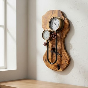 Peut inclure: Une horloge et un thermomètre muraux fixés sur une plaque de bois d'olivier aux bords naturels. L'horloge présente un cadre circulaire en laiton avec des chiffres noirs, tandis que le thermomètre est situé en dessous. Un tuyau en métal sombre relie les deux.