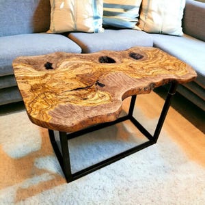 Puede incluir: Mesa de centro de borde vivo con tapa de vetas de madera natural y estructura de metal negro. La tapa de la mesa tiene una forma orgánica única con varios nudos oscuros y una rica paleta de colores cálidos. La mesa mide unos 100 cm de largo.