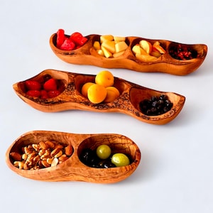 May include: Three wooden serving trays, each with multiple compartments, filled with various fruits and nuts. The trays are made of light brown wood and are filled with red strawberries, yellow apricots, and green grapes.