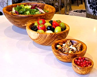 May include: Four wooden bowls of varying sizes, made from olive wood, with a natural wood grain pattern. The bowls are filled with different snacks, including salad, grapes, olives, and nuts.