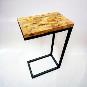 Op de afbeelding: Een bijzettafel met een rechthoekig blad van lichtbruine houten stukken. De tafel heeft een zwart metalen frame. De tafel is 61 cm lang, 30 cm breed en 61 cm hoog.