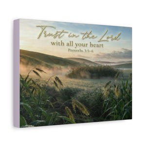 Puede incluir: Un lienzo rectangular para pared que muestra un paisaje de colinas onduladas cubiertas de niebla matutina y hierbas altas. El texto "Trust in the Lord with all your heart Proverbs 3:5-6" está impreso en letras doradas en el cielo.