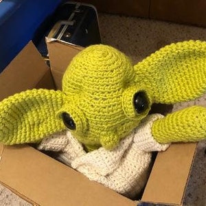 May include: A handmade crochet Yoda hat and costume in a cardboard box. The hat is lime green with large, pointed ears and black eyes. The costume includes a white crocheted top and sleeves.