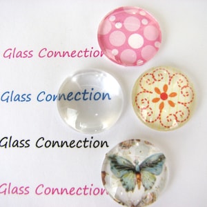 May include: Four round glass cabochons with different designs. One is clear, one has a pink background with white polka dots, one has a yellow background with a red flower and orange stitching, and one has a butterfly design with blue wings.