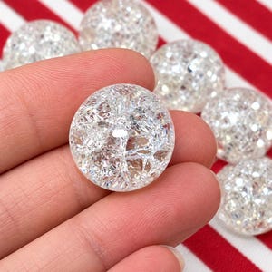 May include: A collection of round, clear glass beads featuring an internal crackle texture that creates a multifaceted, reflective appearance. Each bead has a smooth, polished surface and a spherical shape, showcasing a bright, icy aesthetic.