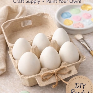 May include: A carton of six blank ceramic eggs, ready for painting. The eggs are in a cardboard egg carton tied with twine. The image includes paint and a paintbrush, with the text "Blank Ceramic Eggs" and "DIY Ready!"