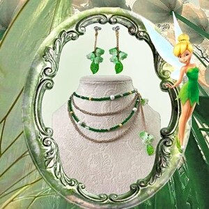 Puede incluir: Un conjunto de collar y pendientes con detalles verdes y dorados. El collar tiene m&uacute;ltiples hilos con cuentas verdes y cadenas doradas. Los pendientes tienen un dise&ntilde;o floral con hojas verdes. Las joyas se exhiben en un maniqu&iacute;.