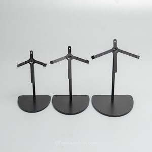 Op de afbeelding: Drie zwarte metalen displaystandaards van verschillende hoogtes, elk met een halfronde voet en een centrale verticale stang met een driepotige steunstructuur aan de bovenkant. De tekst Fossilsonline.com is onderaan in het midden zichtbaar.