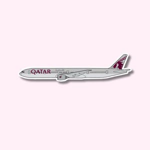Puede incluir: Una pegatina de un avión de Qatar Airways. El avión es de color gris claro con el nombre de la aerolínea en borgoña y escritura árabe. La cola presenta un diseño granate y blanco. La pegatina está sobre un fondo rosa claro.