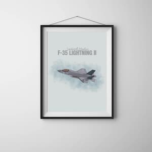 May include: Framed print featuring an illustration of an F-35 Lightning II fighter jet in flight. The artwork is set against a light blue background with a watercolor effect. The text "Lockheed Martin F-35 LIGHTNING II" is displayed at the top.