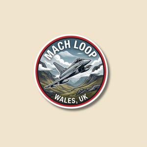 May include: A round sticker featuring a gray jet plane soaring over a mountainous landscape with clouds. The sticker has a red and white border with the text "MACH LOOP WALES, UK" in a circular design.