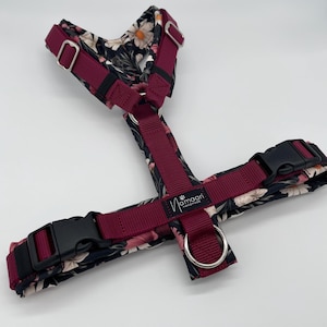 Könnte beinhalten: Ein Hundegeschirr mit floralem Muster in Schwarz, Weiß und Rosa. Das Geschirr hat weinrote Riemen und schwarze Kunststoffschnallen. Der Markenname "mamaari handmade" ist sichtbar.