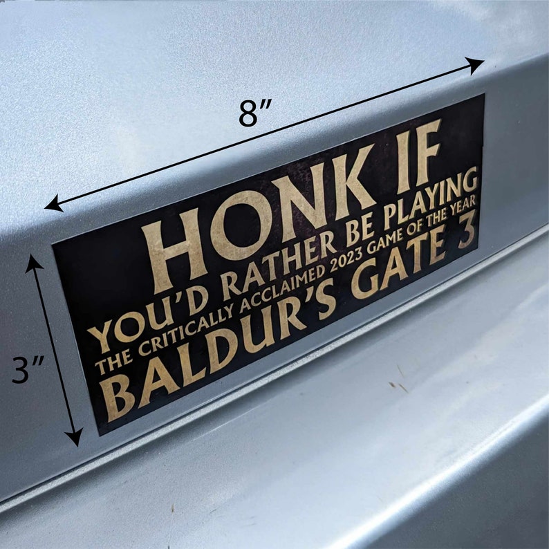 May include: A black rectangular bumper sticker, 8 inches long and 3 inches high, with gold lettering. The text reads "HONK IF YOU'D RATHER BE PLAYING THE CRITICALLY ACCLAIMED 2023 GAME OF THE YEAR BALDUR'S GATE 3."