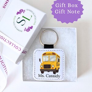 May include: A white gift box with a ribbon and a keychain. The keychain features a yellow school bus design with the text "Ms. Cassidy". The gift box has the text "Gift Collection" and the logo "SL". A purple starburst graphic reads "Gift Box Gift Note".