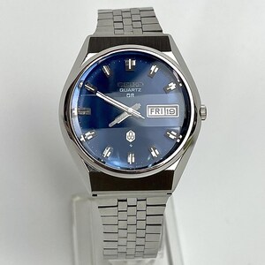 May include: A silver-tone Seiko Quartz QR wristwatch with a deep blue dial, featuring silver hour markers, silver hands, and a day-date window at the three o'clock position displaying FRI 19. The watch has a stainless steel link bracelet.