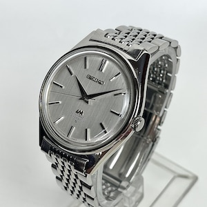 May include: A silver-toned Seiko Lord Matic wristwatch with a brushed metallic dial, silver baton indices, and black hands. The watch features a stainless steel link bracelet and displays the text Seiko, LM, Lord Matic, and 23 Jewels on the face.
