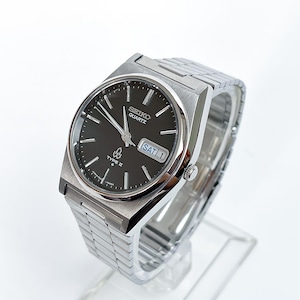 May include: A silver-toned Seiko Quartz Type II wristwatch with a black dial, silver hour markers, and silver hands. The watch features a day-date window displaying SAT 1 and a stainless steel link bracelet with a brushed and polished finish.