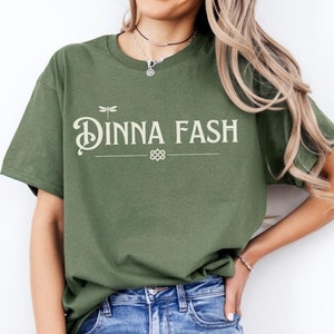 May include: A green t-shirt with the text "Dinna Fash" in a white font with a dragonfly graphic above the text.