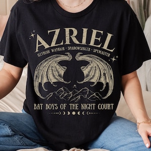 Może przedstawiać: Czarny T-shirt z grafiką w stylu vintage przedstawiającą imię "Azriel", tekst "Elyrian Warrior - Shadowsinger - Spymaster" oraz "Bat Boys of the Night Court". Grafika zawiera również parę skrzydeł nietoperza i półksiężyc.