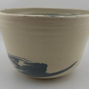 May include: A white ceramic cup with a blue abstract design. The cup has a rounded shape and a smooth, glazed finish.