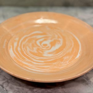 May include: A peach-colored ceramic plate with a white swirl design in the center.