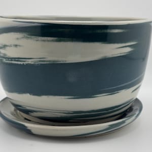May include: A white ceramic planter with a blue and white swirl design. The planter has a matching saucer.