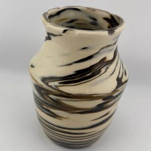May include: A ceramic vase with a cream-colored base and swirling brown and black patterns. The vase has a slightly flared rim and a rounded body. The design gives the vase a marbled appearance. A decorative piece for the home.