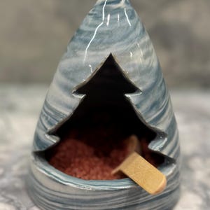 May include: A ceramic incense burner shaped like a mountain with a tree cutout. The burner is glazed in a blue and white swirl pattern. The incense burner has a small wooden spoon inside.