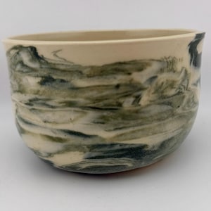 May include: A ceramic bowl with a cream-colored rim and a swirling pattern of green and gray. The bowl's exterior features a marbled effect, creating a unique and artistic design. This handmade bowl is suitable for serving food or as a decorative piece.