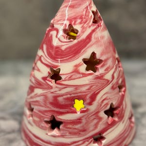 May include: A red and white ceramic cone-shaped candle holder with star-shaped cutouts. The candle holder has a marbled design and is perfect for adding a festive touch to any home.