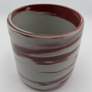May include: A ceramic tumbler with a gray and maroon swirl pattern. The rim and interior are maroon. The cylindrical cup has a smooth, glossy finish. The design is a modern take on a classic drinking vessel.