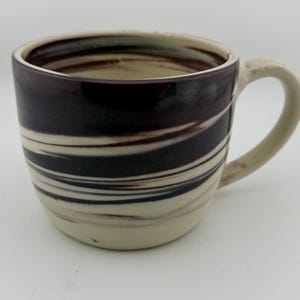 May include: A ceramic mug with a cream-colored handle and base, and a dark brown and cream-colored swirled pattern around the body. The mug has a wide mouth and a rounded shape, suitable for coffee or tea.