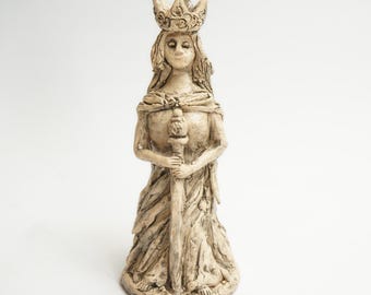 May include: A ceramic figurine of a queen wearing a crown and holding a scepter. The figurine is painted in a cream color and has a detailed design.
