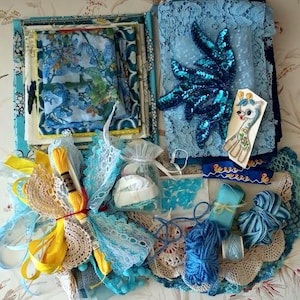 May include: A collection of blue and yellow craft supplies including fabric squares, lace trim, a sequined applique, a giraffe patch, embroidery floss, yarn, ribbon, and a small organza bag containing beads and white fabric pieces for sewing projects.