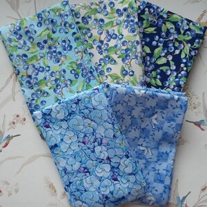 May include: Five fabric swatches in various shades of blue with different patterns. The patterns include blueberries, flowers, and a geometric design.