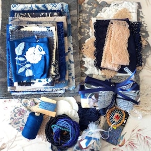 May include: A collection of craft supplies including stacks of blue and white patterned fabric squares, assorted lace trims in beige and navy, spools of blue thread, a bundle of blue beads, and a small bag of buttons with a decorative embroidered patch.