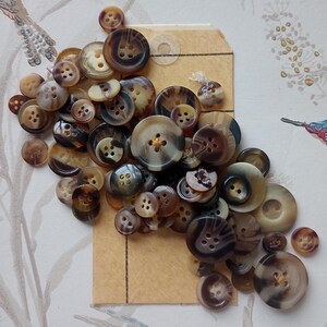 May include: A collection of brown and black buttons with a mottled pattern. The buttons are arranged on a brown paper tag.