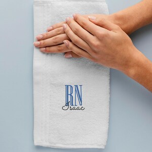 May include: White hand towel with blue embroidered letters "RN" and the name "Isaac" below.