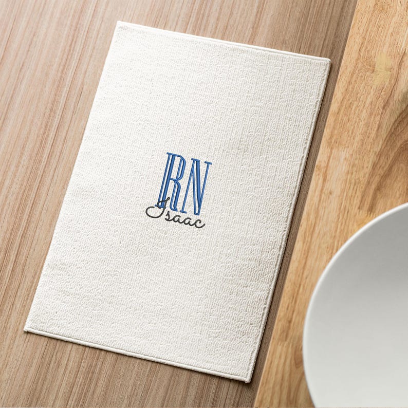 May include: White placemat with blue embroidered initials "RN" and the name "Isaac" underneath.