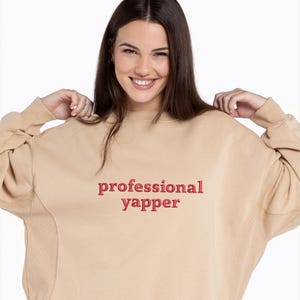 May include: A tan sweatshirt with the text "professional yapper" in red embroidered on the front.